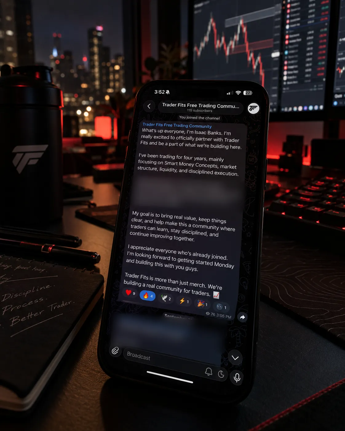 Isaac's welcome message in the Trader Fits Free Trading Community on Telegram, shown on a phone at a trading desk